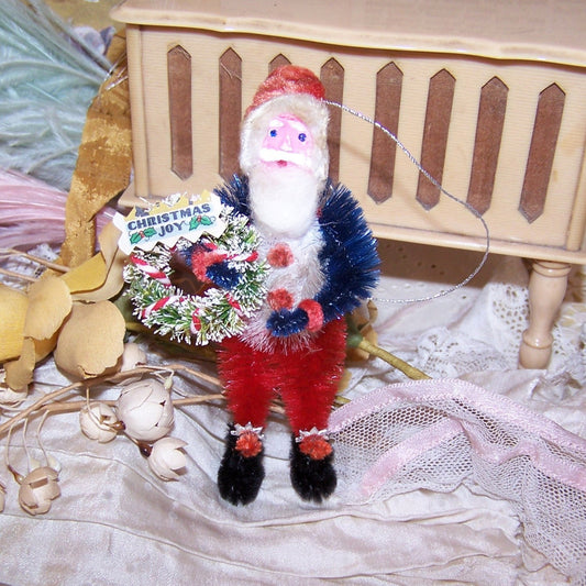 Red, White & Blue patriotic chenille ornament of Santa Claus.  In a retro inspired design, Santa carries a bottlebrush wreath; sentiment is Christmas Joy!