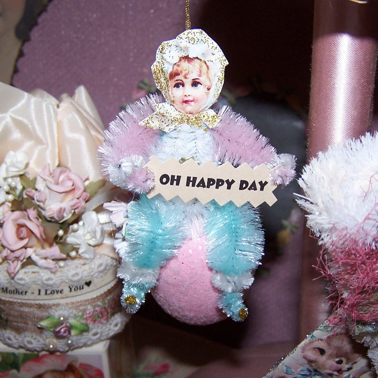 Handcrafted Victorian Revival chenille ornament for Spring. A little girl sits on a sparkly Pink Egg and holds a sign that reads OH HAPPY DAY. All occasion gift