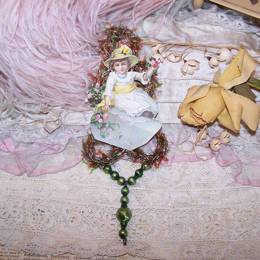 Victorian Revival handcrafted tinsel and mercury glass Christmas ornament.  Die cut of a Lady in white holding flowers is the focal point. Light but lengthy.
