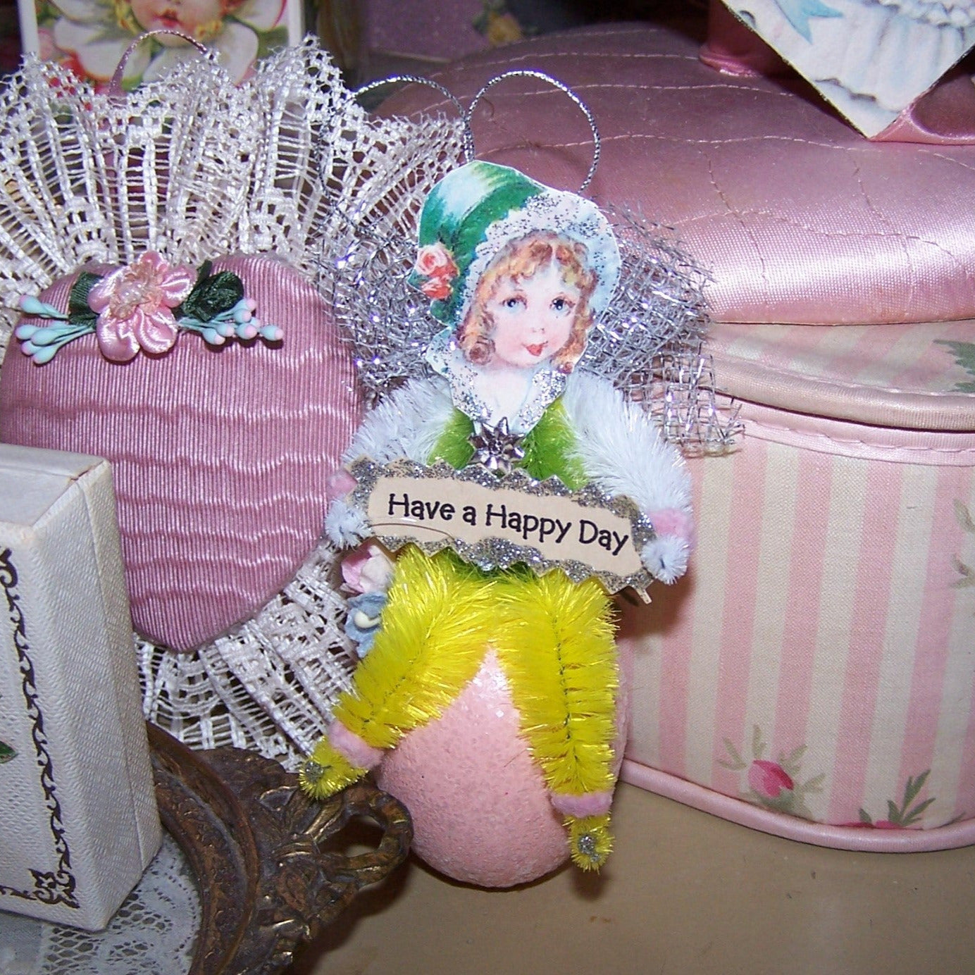 Victorian Revival Spring chenille ornament. A sweet faced girl sits on a sparkly Pink Egg and holds a sign that reads HAVE A HAPPY DAY. All occasion gift idea!