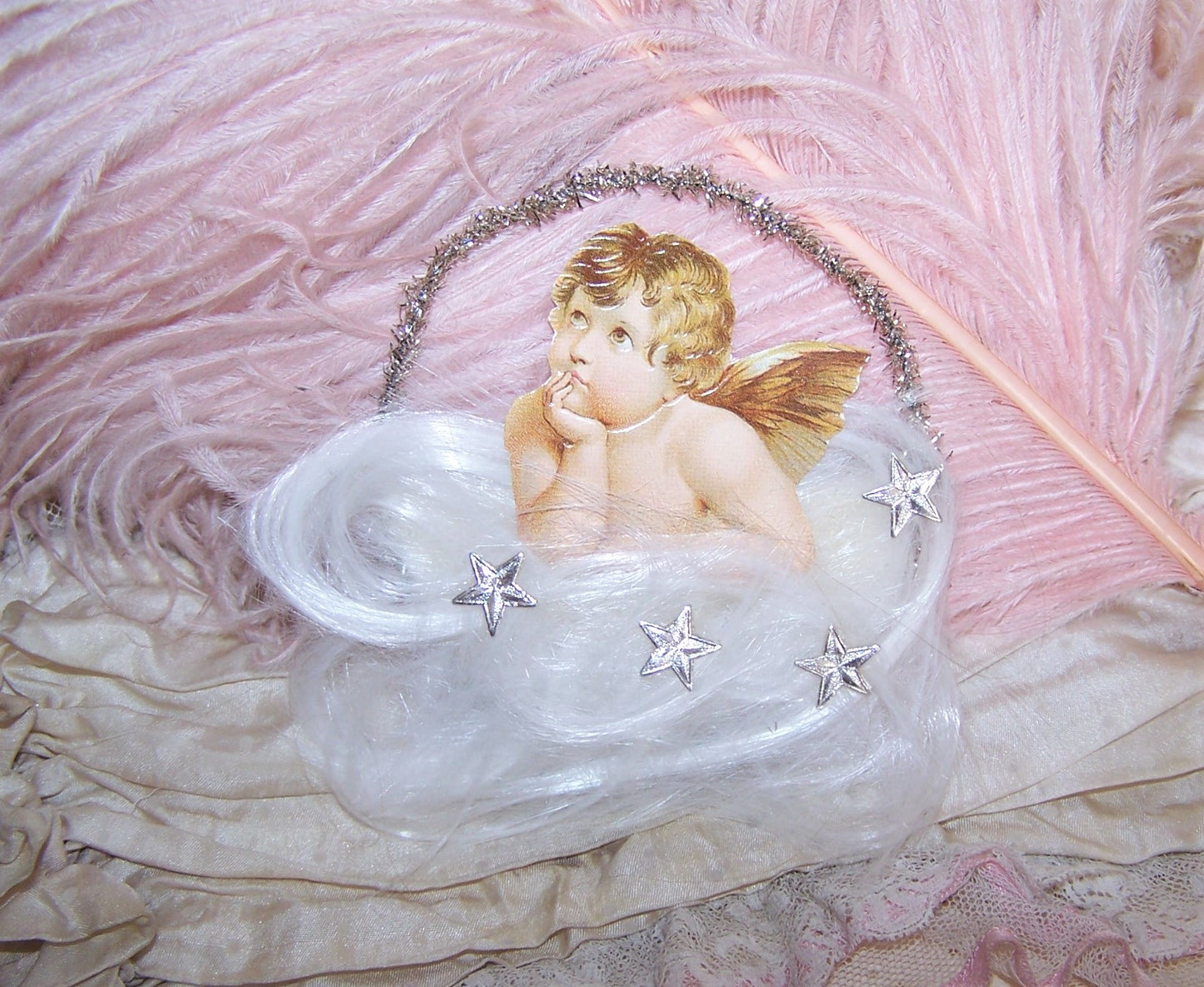 Victorian Revival holiday ornament of Raphael's angel peeking down from a cloud of spun glass and silver Dresden stars. Silver tinsel hangar; white felt back.