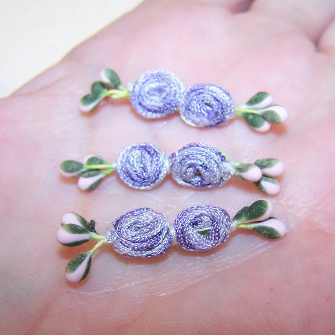 With a pair of center rounds made of coiled ombre ribbon, this set/3 hand sewn florals have pink and green sugar pips. Length is 1-1/2"; width is 1/4". 