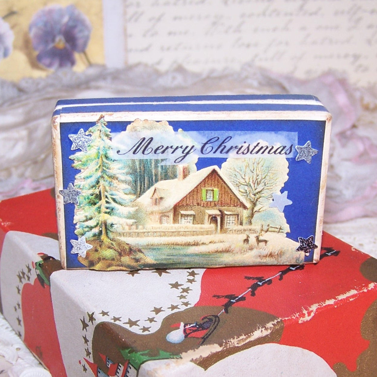 Vintage pharmacy pill box with a Christmas theme. Top design is an Antique Victorian die cut of a log cabin winter scene; sentiment is MERRY CHRISTMAS. 