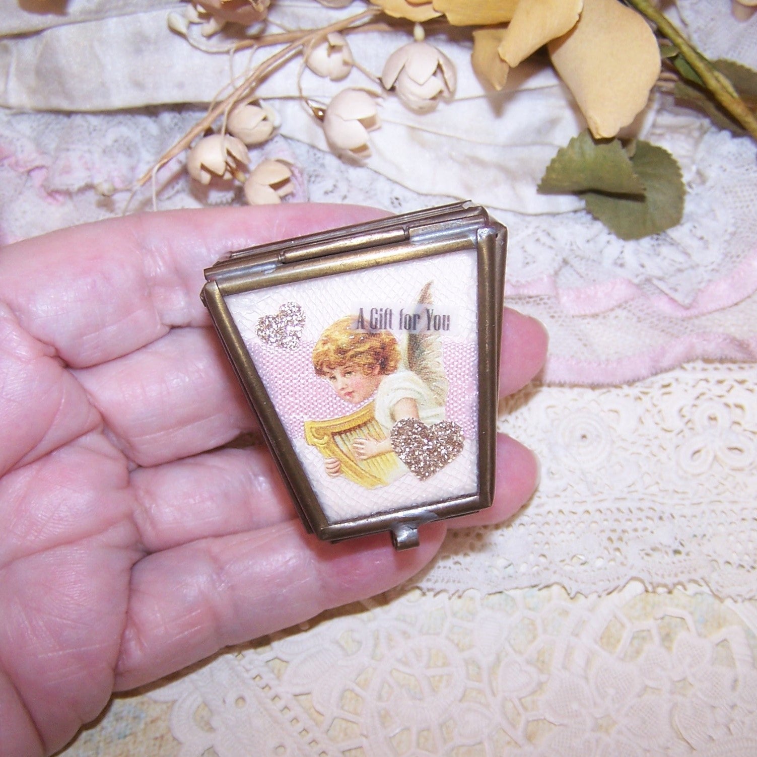 Repurposed brass trinket box with glass panels upcycled with pink cardstock, repro Victorian angel/flower die cuts, ribbons, cording and gold glitter stars.
