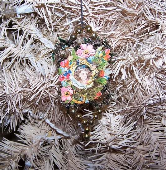 Victorian Revival handcrafted tinsel and mercury glass Christmas ornament.  Die cut of a young girl in white surrounded by cherry blossoms. Light but lengthy.
