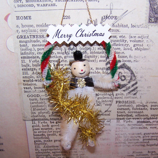 Vintage spun cotton, chenille and gold tinsel holiday ornament.  Frosty the Snowman carries a Merry Christmas banner.  Cord at back for hanging on a tree.